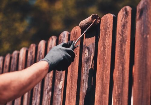 Diligent man is painting fence with brush